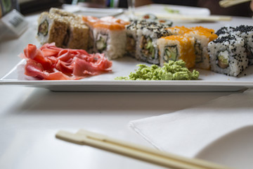 Set of sushi rolls with vasabi and ginger on a white plate.o