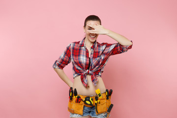 Handyman woman in shirt, denim shorts, kit tools belt full of variety useful instruments cover eyes with hand isolated on pink background. Female doing male work. Renovation and occupation concept.