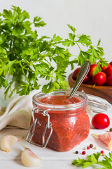 Tkemali sauce from red plums and ingredients for cooking garlic, parsley, dill, pepper with copy space on a light wooden background