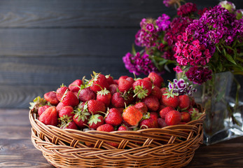 Ripe sweet strawberries in wicker basket and wildflower on wooden background