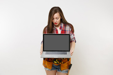 Naklejka premium Woman in kit tools belt full of variety instruments holding laptop pc computer with blank black empty screen display monitor isolated on white background. Female doing male work. Renovation concept.