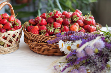 Strawberries in basket on wooden background with wildflower.