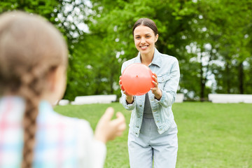 Happy young woman with red balloon or ball playing with her little daughter in natural environment