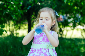 cute little kid girl drinks water from a bottle in summer park