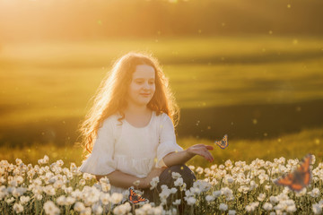 Curly hair girl with a butterfly on his hand on meadow outdoors.