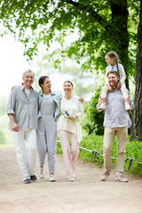 Cheerful family in casualwear walking down road in natural environment during chill