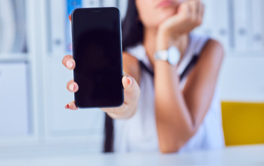 Young sad woman showing a blank smartphone screen. Focus on smartphone. Free space for your message.
