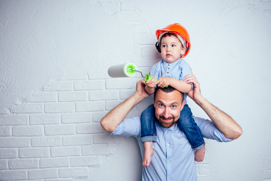 happy family handsome father and charming cute little son in helmet hardhat painted wall with paint white color . concept of repairs house ( apartment ) by young family