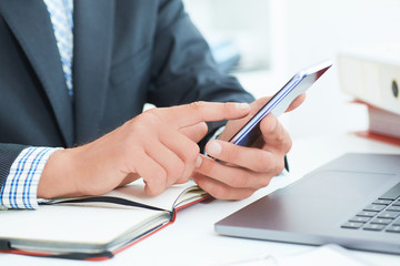 Businessman in black suit using mobile smart phone and working on laptop computer close up. Just...