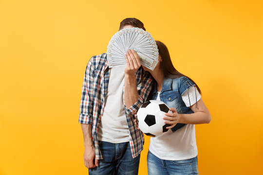 Young win couple, woman man, football fans holding bundle of dollars, cash money, soccer ball, cheer up support team isolated on yellow background. Sport bet, excitement ardor family lifestyle concept