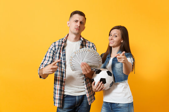 Young win couple, woman man, football fans holding bundle of dollars, cash money, soccer ball, cheer up support team isolated on yellow background. Sport bet, excitement ardor family lifestyle concept