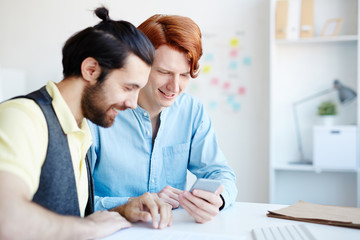 Two young men reading or discussing curious notification in smartphone of one of them