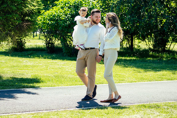Obraz premium happy and stylish family are walking in the summer in the park. beautiful woman, stylish man and cute girl looking and smile copyspace