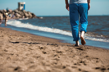 Back view of low section of barefoot man moving along coastline on wet sand