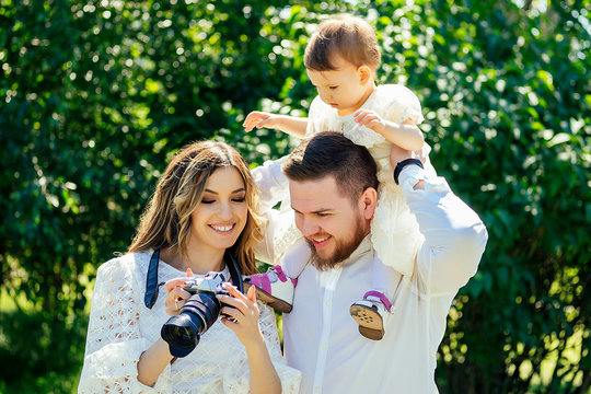 happy and stylish family in the summer park. family photosession woman photographer photographing bearded husband and cute daughter looking watching photos at camera