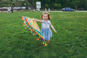 Laughing little cute child baby girl in denim dress running, play with colorful kite and have fun in green park. Mother, little kid daughter. Mother's Day, love family, parenthood, childhood concept.