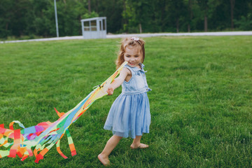 Smiling little cute child baby girl in denim dress walking, play with colorful kite and have fun in green park. Mother, little kid daughter. Mother's Day, love family, parenthood, childhood concept.