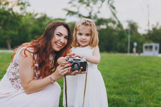 Joyful woman in light dress and little cute child baby girl holding retro vintage photo camera in green park. Mother, little kid daughter. Mother's Day, love family, parenthood, childhood concept.
