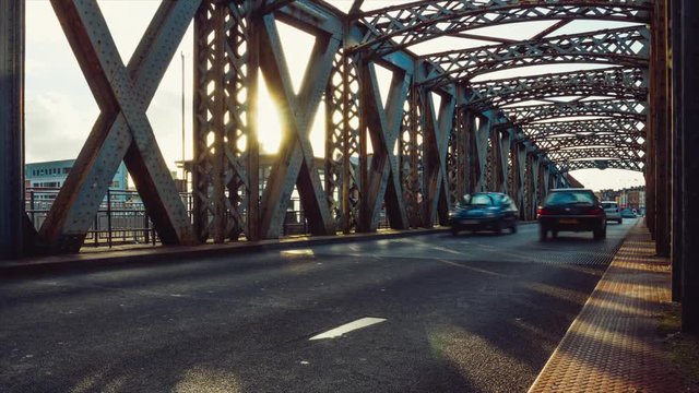 Time lapse of cars driving on the asphalt road of the city bridge on a sunny day in Dieppe, France. Metal structure of an old bridge tunnel. Urban scene, city life, transport and traffic concept