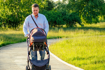 handsome man is walking with a baby in a stroller in the park