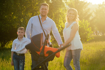 Obraz premium active big happy family father, mother, son and baby in stroller walking in the park