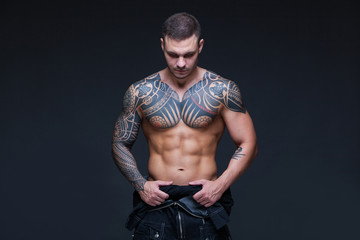 The man with a muscular naked torso with tattoos on the dark background. ABS