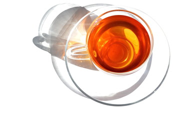 glass transparent cup of warm tea and dish in morning bright rays sunlight with shadow on white...