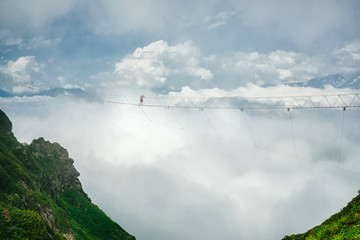 Extreme entertainment in the mountains. A person goes a long way along the suspended bridge against...