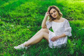 Naklejka na ściany i meble Young beautiful blonde girl in white dress with a flower tulip on a background of green grass