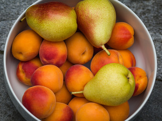 Fototapeta na wymiar Ripe apricots and pears in a white bowl. Fresh fruits. Top view of a close-up.