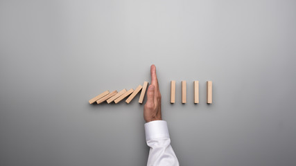 Male hand in white shirt stopping falling dominos on gray desk