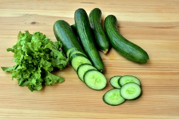 Fresh cucumbers and salad leaves on a wooden table.