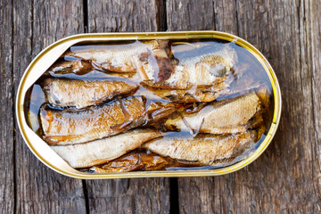 Open tin can of sprats on rustic wooden table