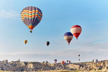 Fototapeta premium Large number of balloons fly in morning in the sky in rays of the dawn sun. Balloons balloons in the sky in the clouds above the mountains. Main attraction of Cappadocia, Turkey. Fabulous view