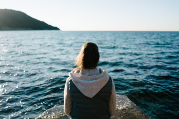 Close up shot of a young woman sitting on a rock, gazing in the distance, looking in the sea.