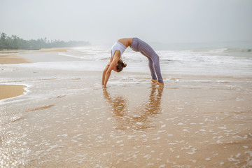Caucasian woman practicing yoga at seashore of tropic ocean