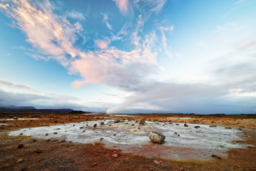 Wide view over a volcanic landscape with reddish and light gray ground, rising steam, above it a sky with a red cloud formation - Location: Iceland, geothermal area 'Hverarönd' near the lake 'Myvatn'