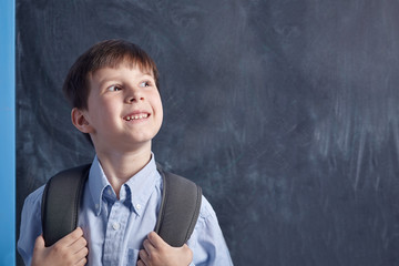 Thoughtful Caucasian schoolboy with backpack against blackboard.