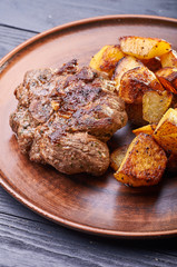 Appetizing piece of fried meat on a large clay plate. Fried potatoes with crispy crust on garnish. Tables are served for lunch and dinner at home, in a restaurant, in the cafe.