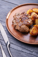 Appetizing piece of fried meat on a large clay plate. Fried potatoes with crispy crust on garnish. Tables are served for lunch and dinner at home, in a restaurant, in the cafe.