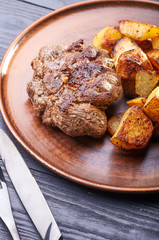Appetizing piece of fried meat on a large clay plate. Fried potatoes with crispy crust on garnish. Tables are served for lunch and dinner at home, in a restaurant, in the cafe.