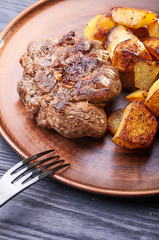 Appetizing piece of fried meat on a large clay plate. Fried potatoes with crispy crust on garnish. Tables are served for lunch and dinner at home, in a restaurant, in the cafe.