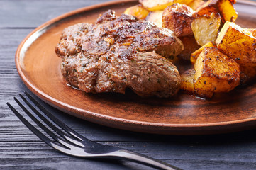 Appetizing piece of fried meat on a large clay plate. Fried potatoes with crispy crust on garnish. Tables are served for lunch and dinner at home, in a restaurant, in the cafe.