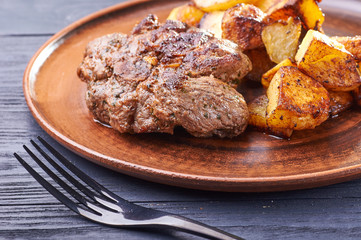 Appetizing piece of fried meat on a large clay plate. Fried potatoes with crispy crust on garnish....