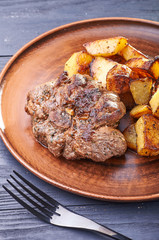 Appetizing piece of fried meat on a large clay plate. Fried potatoes with crispy crust on garnish. Tables are served for lunch and dinner at home, in a restaurant, in the cafe.