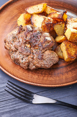 Appetizing piece of fried meat on a large clay plate. Fried potatoes with crispy crust on garnish. Tables are served for lunch and dinner at home, in a restaurant, in the cafe.