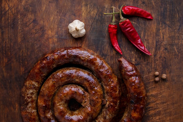 Grilled ring of homemade sausage is on a wooden board with pepper and garlic