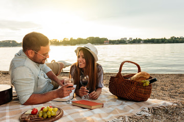 Young couple relaxing at the beach. Lying on the blanket, reading books and drinking wine. Sunset...