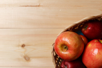 Ripe red apples in a basket on a bright wooden background. Top view