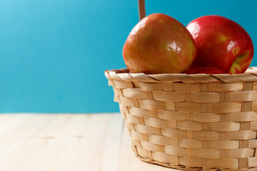 Ripe red apples in a basket on a bright wooden background